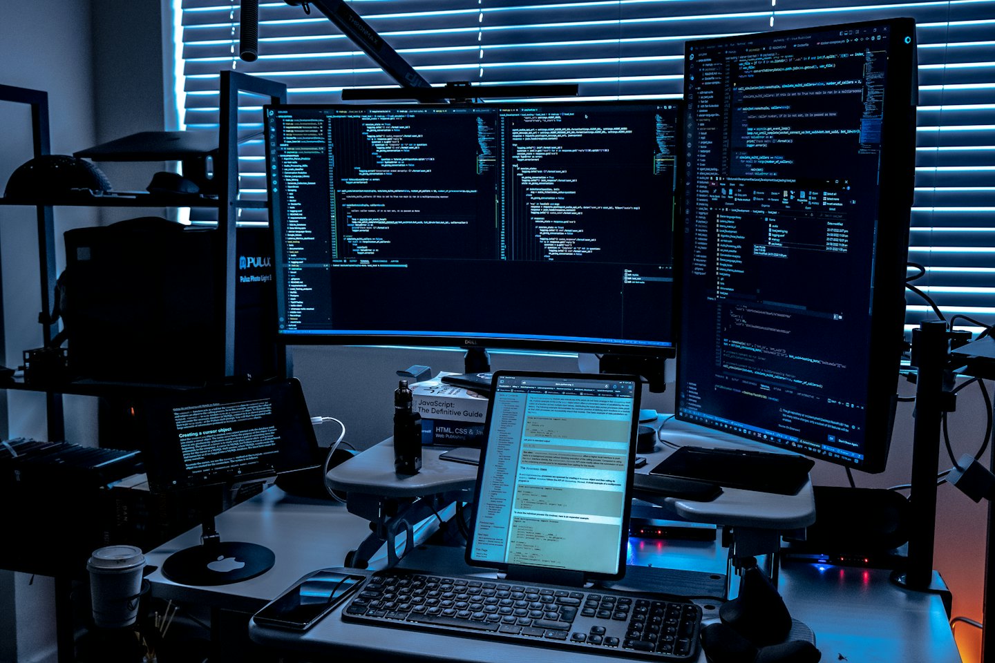 Two large monitors and a laptop showing code in a dark workspace.